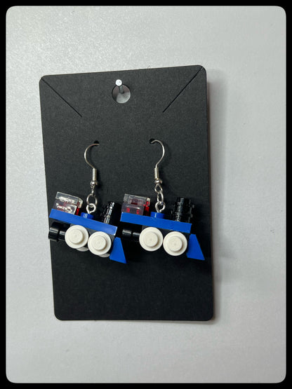Pair of train-themed earrings on a black card against a gray background