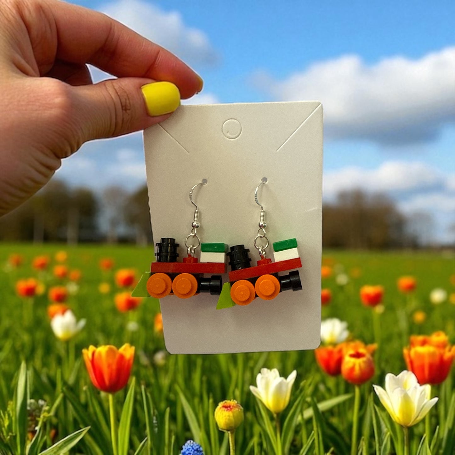 Earring display card with train-themed earrings held by a hand against a field of tulips.